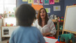 © Krakenimages.com - Woman teacher with boy gestures toward plush elephant on table and papers by whiteboard in building; encouragement early learning.