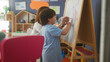 © Krakenimages.com - Woman teacher guides little boy as he draws hearts on easel whiteboard, holding marker and pointing to shapes in a preschool classroom; encouragement early learning.