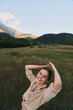 © SHOTPRIME STUDIO - A smiling woman enjoys outdoor lifestyle in a field with distant mountains, capturing a carefree moment in nature in a sunlit meadow, wearing casual attire.