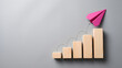 © Rafli - Business Growth and Success Concept Featuring a Pink Paper Airplane Soaring Above Wooden Blocks