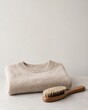 © JS - Clothing care concept shows Folded gray sweater with a wooden brush on a light surface against a plain background.