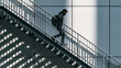 © kora studio - Person ascends staircase, dressed in casual attire, with backpack. scene features strong geometric lines and shadows created by architecture, emphasizing modern urban environment