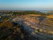 © Amazing Aerial - Aerial view of TPA Suwung landfill with excavators working on large waste piles, surrounded by mangrove forests and urban landscape in Kecamatan Denpasar Selatan, Bali, Indonesia.