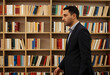 © Pixel-Shot - Academic research and intellectual development, man in suit walking past library bookshelves for professional growth and education in a university setting