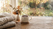© Liza - A warm cozy scene featuring a steaming ceramic mug of tea beside a stack of knitted sweaters and dried autumn foliage on a wooden table