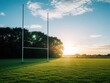 © Lubov - Tall rugby goal post stands on green grass pitch at sunset. White posts reach towards blue sky with clouds. Sun flare shines over field near dark trees. Empty sports ground in Ireland ready for