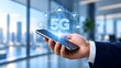 © Andi - Hand holding smartphone displaying glowing 5G network icons and symbols representing connectivity and digital communication in a modern office with city skyline background
