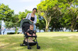 © leungchopan - Mother pushing baby stroller in green park