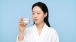 © XiangAn - Young Asian woman holding a skincare cream jar against a blue background