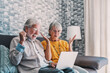 © Daniel - An elderly couple react with joyful surprise and excitement while looking at a laptop on the sofa, sharing a happy moment of online success, video call or digital discovery in their cozy home.