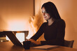 © Daniel - A young woman types on a laptop at a warmly lit desk, focused and calm while working remotely in the evening with a notebook and coffee nearby, conveying productivity and concentration.