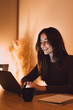 © Daniel - A young woman smiles as she types on a laptop in a cozy, warm-lit home office at night, enjoying focused remote work with a coffee mug and notebook nearby for a relaxed productivity vibe.