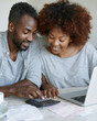 © lashkhidzetim - Couple shares joyful moment reviewing finances together. Their smiles reflect confidence and teamwork. Hands gently press calculator keys near laptop. Paper bills and coffee cup add everyday realism