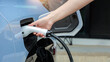 © Piya W. - Hand holding plug for fast ev charging process to refuel modern electric car outdoors with convenient power connection
