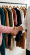 © miss irine - Two diverse people shake hands in fashion boutique. One person wears pink sweater wears white shirt. Reach agreement celebrate purchase near clothing rack with colorful apparel. Business deal