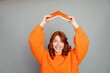 © deagreez - Smiling redhead woman in bright orange sweater holding an orange book over her head, playful portrait conveying joy, reading, creativity, confidence and upbeat energy
