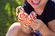© Austockphoto - Happy little girl holding red and white striped candy cane lollies at Christmas outdoors
