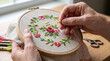 © Angavlan - Hands craft intricate floral embroidery on linen fabric, held in wooden hoop. Detailed embroidery project involves colorful threads, needle, skilled stitching. Inspiring artistic expression,