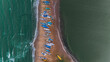 © hasan - Top-down aerial view of colorful fishing boats lined up on a narrow sandy beach spit separating two contrasting ocean waters.