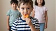 © YiuCheung - Young boy enjoys lollipop, two friends watch in soft focus behind him.