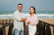 © Елена Попова - Mature couple posing on a wooden boardwalk at the beach, looking at the camera with arms crossed, representing a harmonious partnership and carefree holiday by the sea