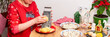 © pundapanda - A woman in a festive shirt grates potatoes at her kitchen table to make the Christmas salad Shuba, herring under fur coat. Plates with herring, beets, and other ingredients are nearby for preparation