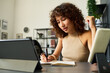 © Mediaphotos - Young female designer writing in notebook while working with tablet in creative agency studio. Imagery suitable for digital marketing and branding campaign