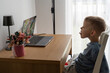 © Maryia - Young boy practices a tongue exercise during an online speech therapy session on a laptop at home. Concept of remote speech development, articulation training and accessible support for children.