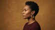 © Svitlana - Black woman shown in elegant side profile against a warm ochre-brown studio background, premium editorial portrait photography, short natural hair, burgundy top and hoop earring, sculpted cheekbone