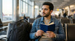 © SUMIDAH - Young man waiting at an airport terminal reading a book with a backpack beside him during travel leisure moments