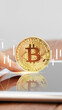 © fotofabrika - Bitcoin coin held above a tablet with stock market data in the background
