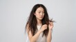 © Yellyana - Asian woman examining dry, frizzy and damaged hair against a clean studio background, expressing concern about split ends and hair condition. Suitable for shampoo advertising, haircare campaigns, beau