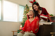 © Natee Meepian - Asian daughter surprising senior mother with Christmas gift box at home