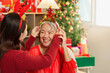 © Natee Meepian - Asian daughter adjusting Christmas tree headband on senior mother close up