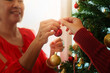 © Natee Meepian - Close up of hands decorating Christmas tree with red ornament