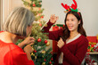© Natee Meepian - Happy Asian daughter showing Christmas ornament to mother at home