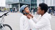 © AI-Universe - Mother adjusting the chin strap of her son's bicycle helmet outdoors