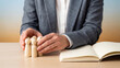 © NK - Employee protection and staff care concept, businessman covering group of wooden people figures with open blank notebook for HR support, insurance, leadership, trust and company welfare