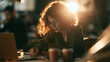 © haemye - Focused female manager writing notes near a laptop and coffee cups under warm golden backlighting, concept for corporate finance, project management and remote work