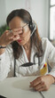 © Krakenimages.com - Woman doctor in building touches temple with hand while wearing stethoscope and headset at clinic desk, looking down; fatigue care.