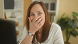 © Krakenimages.com - Middle age woman laughing with hand covering mouth at a computer desk in a building; joyful warm connection.
