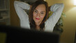 © Krakenimages.com - Middle aged woman at computer with eyes closed stretching arms late at night in a home studio with bookshelf and plant visible; calm focus productivity.