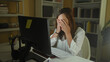© Krakenimages.com - Woman at computer reading printed papers with hands on temples at desk in office building; late work fatigue.