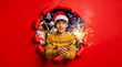 © ZaStock - Young man wearing santa hat and reindeer sweater holding sparkling sparkler through torn red paper, festive holiday celebration, winter magic.