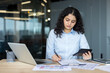 © Liubomir - Businesswoman calculating finances and analyzing paperwork in office