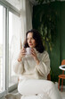 © Felix & Mary/Stocksy - Woman Holding a Cup While Sitting in a Bright Room With Plants