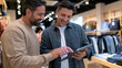 © CinimaticWorks - two smiling men in white t shirts talking and reviewing papers in a clothing store with garments hanging on racks showing retail business and friendly customer service