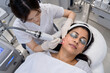 © Vexora Stocks - Female practitioner treating South Asian woman's cheek with red light laser handpiece, high angle view in clinic