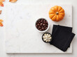 © Pimaksorn - Flat lay of halloween candy station with chocolate almonds white chocolate raisins orange pumpkin and black napkins on white marble board with autumn leaves