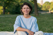 © Eva Corbella - Woman sitting on grass in a park wearing a blue striped shirt and light pants during a sunny day